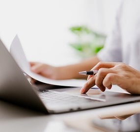 hands on computer holding pen and paper